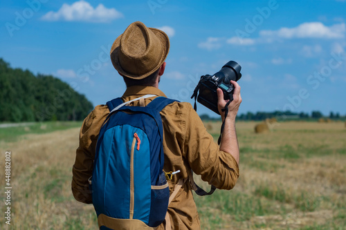 Traveler photographer with a camera in his hand against the background of a field and haystacks.