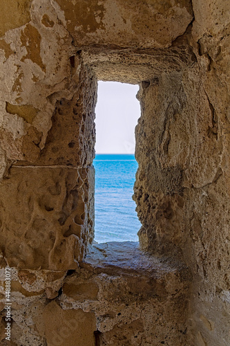 A view of the sea through the loophole of a medieval fort in the southern part of the Finikoudes embankment on the island of Cyprus. The fort is located in the city of Larnaca.