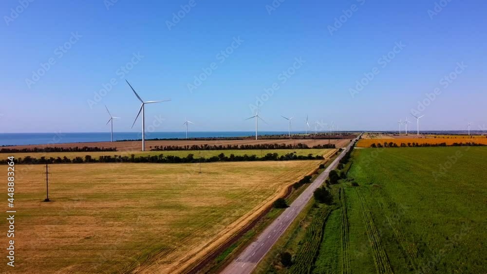 Aerial drone view of a flying over the wind turbine and agricultural fields. Windmills on the background of the sea. Sunflower field. Windmill. Wind farm. Aerial drone view of a flying over the wind turbine and agricultural fields. Windmills on the background of the sea. Sunflower field. Windmill. Wind farm.