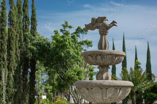 Fuente con figura de ángel con arboles y el cielo azul al fondo