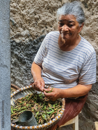 Aged African American woman shelling beans while sitting on street