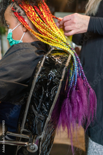 Masked girl getting lomg rainbow box briaids installed photo
