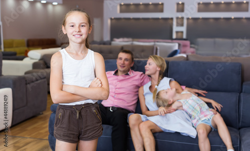 Postrait of happy child girl is standing near new sofa in furniture shop photo