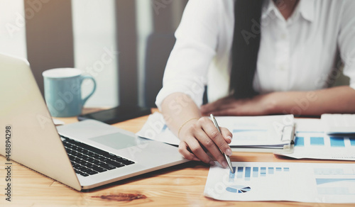 Close up Businesswoman hand holding pen and pointing at financial paperwork, financial charts to analyze profit concept