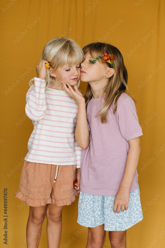 Portrait of two little girls over yellow backdrop Portrait of two little girls over yellow backdrop