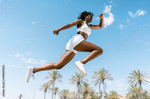 Active black sportswoman jumping against blue sky