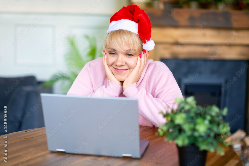 Young woman in Santa hat in front of laptop monitor. Online meeting with friends or family on the eve of Christmas or New Year. Young woman in Santa hat in front of laptop monitor. Online meeting with friends or family on the eve of Christmas or New Year.
