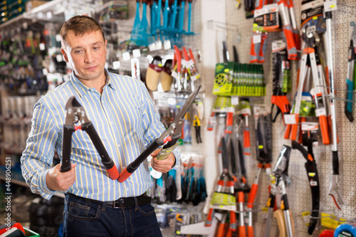Happy positive male customer examining secateurs in garden equipment shop