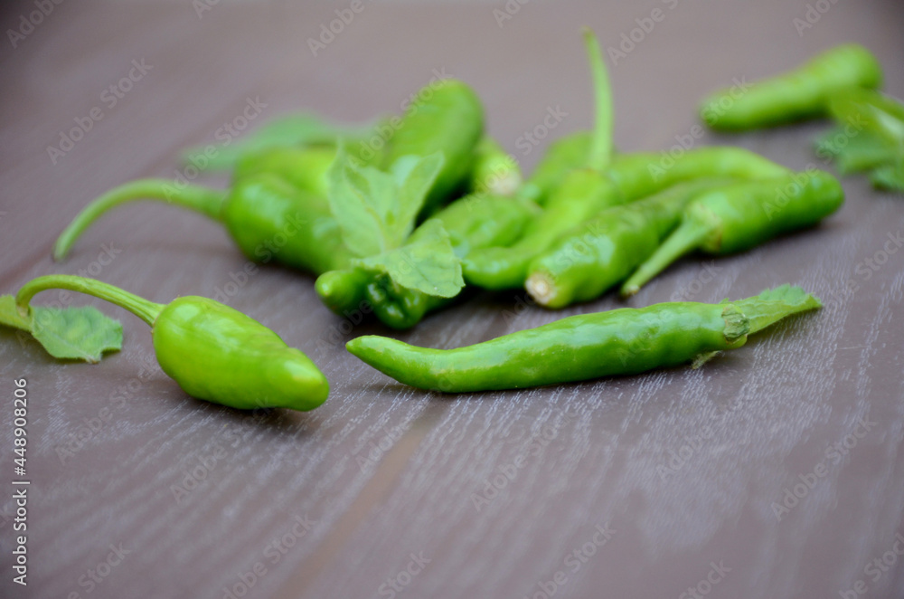 closeup the bunch ripe green chilly with mint leaves over out of focus brown background. closeup the bunch ripe green chilly with mint leaves over out of focus brown background.