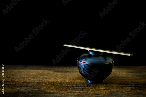 Black cup with chopsticks Japanese style on wooden floor with black background.