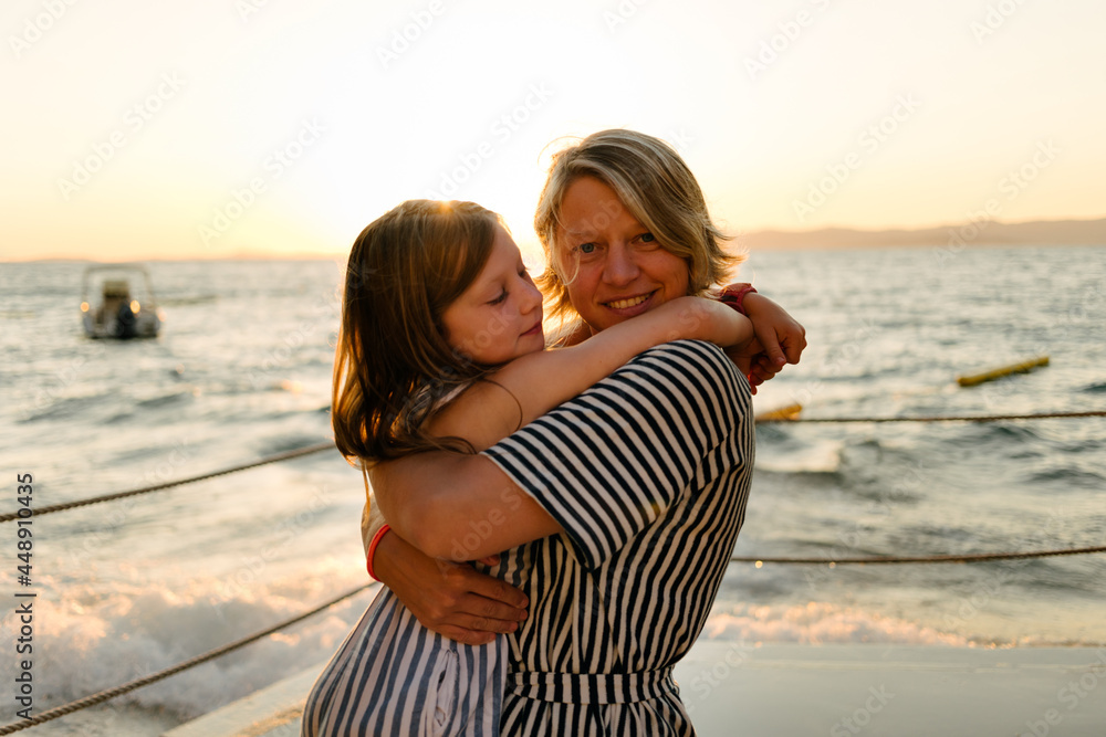 Mother and daughter having tender moment hugging each other at sea - family of single mother concept Mother and daughter having tender moment hugging each other at sea - family of single mother concept