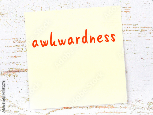 Yellow sticky note on wooden wall with handwritten word awkwardness