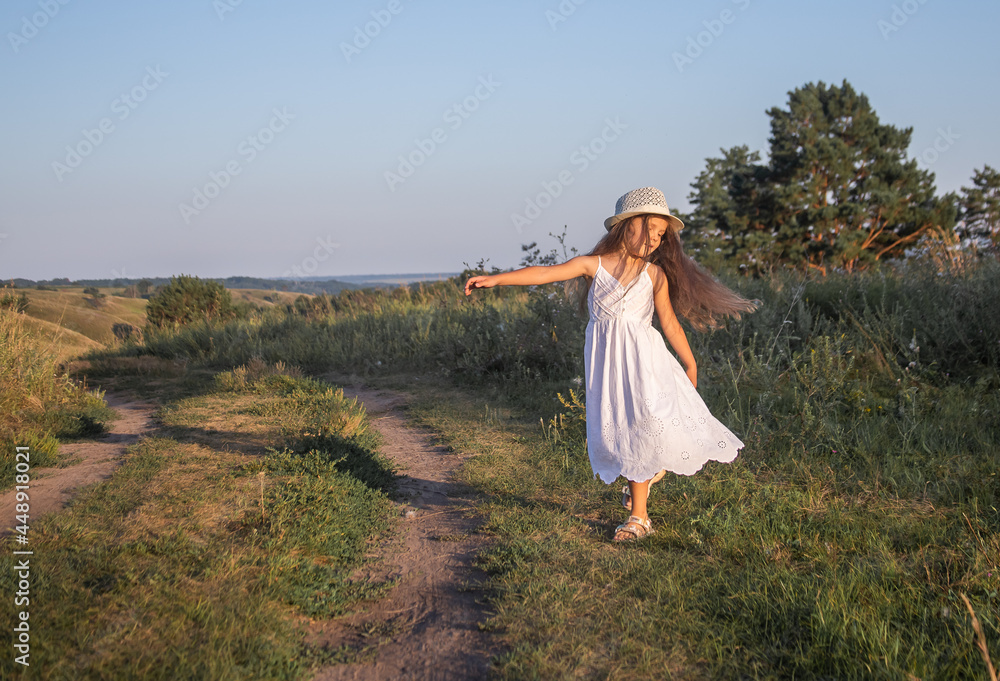 
Little happy girl in a white dress runs on rural roads, childrens tourism, school holidays.
