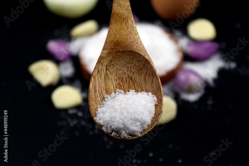 Zoomed salt on the wooden spoon with seasoning onion in black background