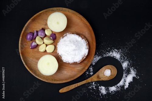 Vintage wooden plate and spoon have ingredients onion salt in black background