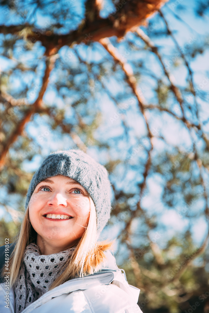 Young Caucasian Lady Woman Dressed In White Jacket And Grey-blue, Gray Hat Posing Near Pine Tree. Close Up Portrait. beautiful young woman smiling Young Caucasian Lady Woman Dressed In White Jacket And Grey-blue, Gray Hat Posing Near Pine Tree. Close Up Portrait. beautiful young woman smiling