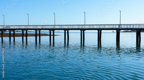 A view of Victoria Point jetty reflected in the rippled water beneath, on a clear blue day
