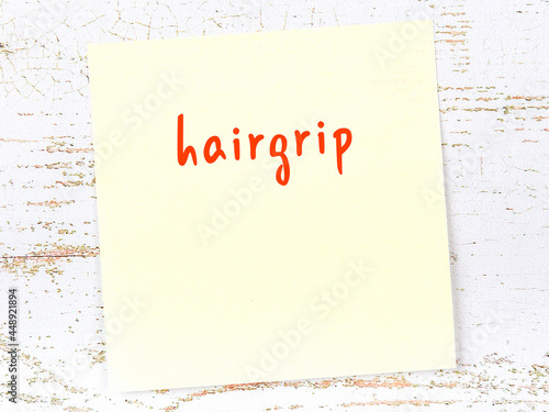 Yellow sticky note on wooden wall with handwritten word hairgrip