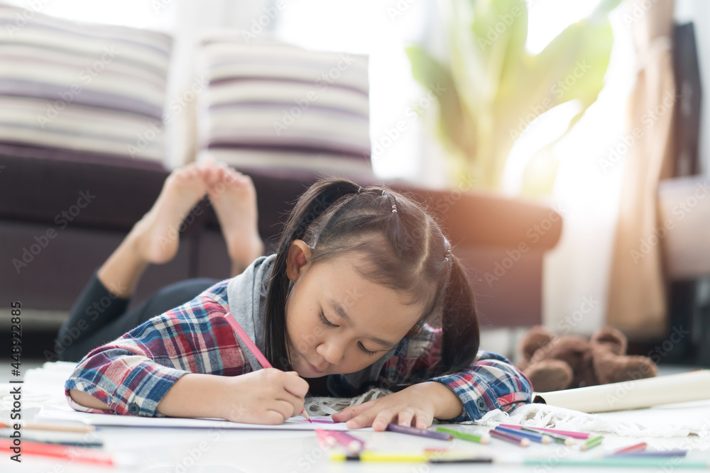 Happy cute asian little girl drawing using colorful pencils while lying on the floor at home Happy cute asian little girl drawing using colorful pencils while lying on the floor at home