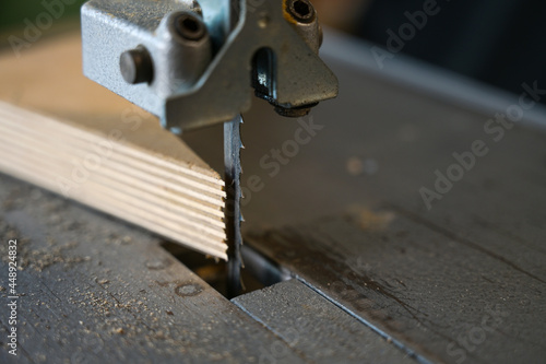 Detail of the saw blade of an electric bandsaw and a multiplex wood panel in a workshop, copy space, selected focus, narrow depth of field photo