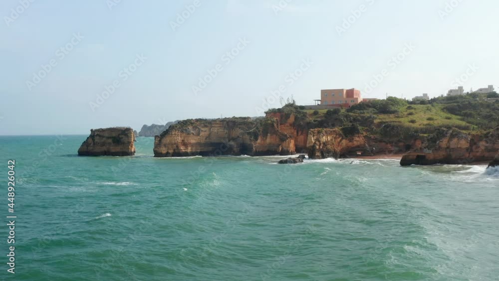 Aerial drone view of waves crashing against colorful Lagos cliff coastline, drone flying foward above rocky coast reveal amazing sea landscape, day Aerial drone view of waves crashing against colorful Lagos cliff coastline, drone flying foward above rocky coast reveal amazing sea landscape, day