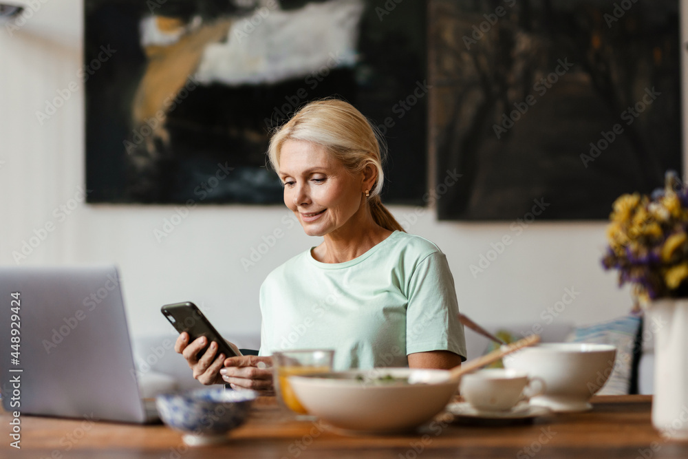 Blonde mature woman using laptop and cellphone while having lunch Blonde mature woman using laptop and cellphone while having lunch