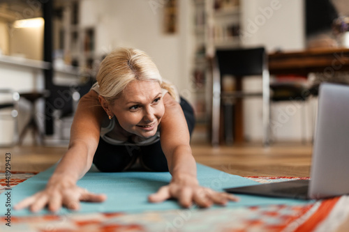 Blonde mature woman smiling and using laptop during yoga practice