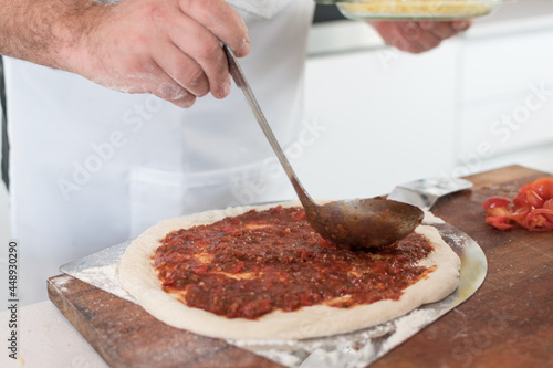 фотографія Closeup shot of male cook floury hands spreading the sauce on the dough, pizza m