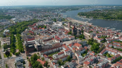 Forwards fly above town. Aerial view of city at river or sea bay. Tilt down footage of Neuer Markt square with gabled houses and Saint Mary church photo