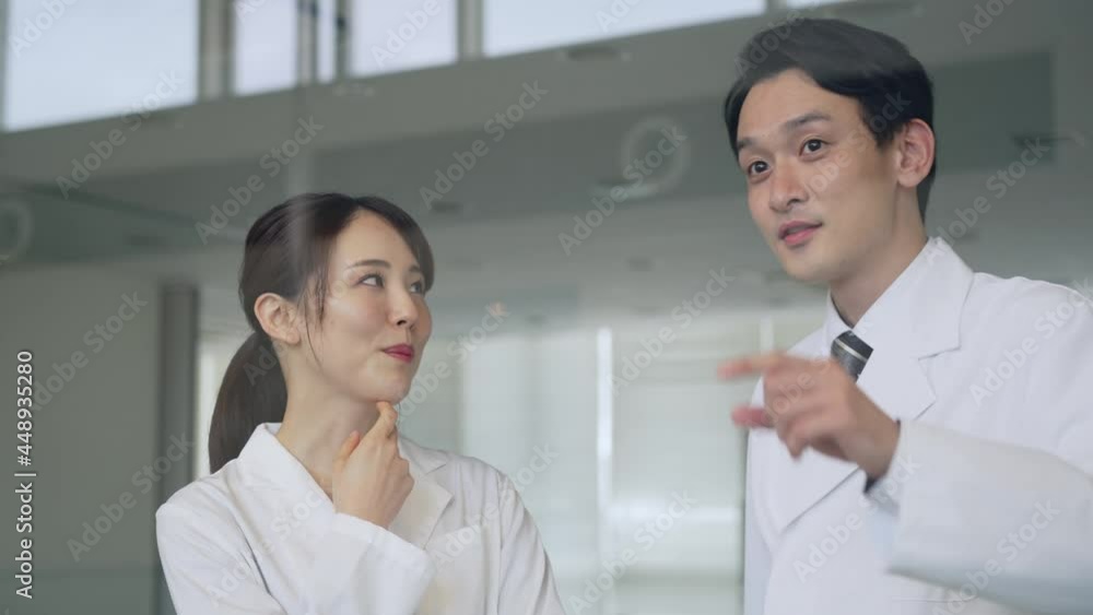 ガラスから外を見ながら会話する白衣の男女 ガラスから外を見ながら会話する白衣の男女