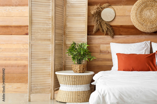 Houseplant on bedside table and folding screen near wooden wall in bedroom
