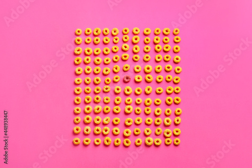 Pink cereal ring among yellow ones on color background. Concept of uniqueness