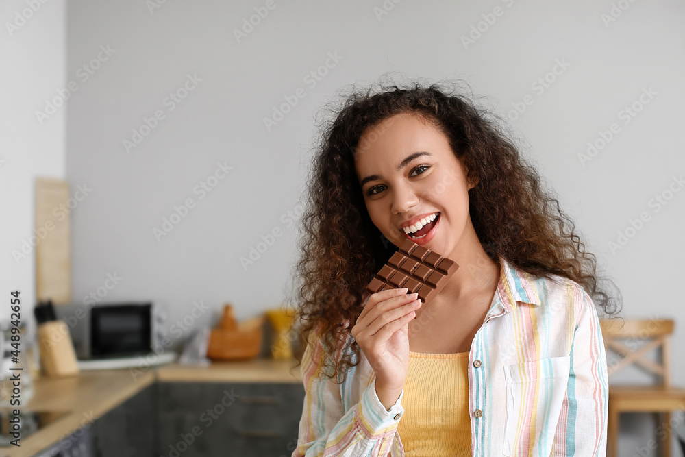 Young African-American woman eating chocolate in kitchen Young African-American woman eating chocolate in kitchen