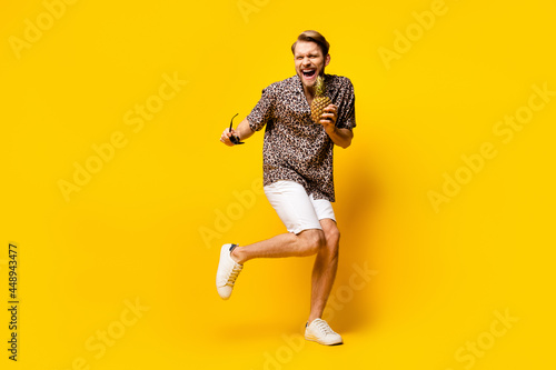 Full length photo of cute funky young guy wear leopard outfit arm dark eyewear pineapple dancing isolated yellow color background