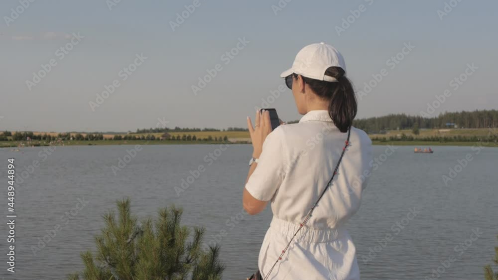 Young woman in white baseball cap taking a picture of the lake at sunset. Young woman in white baseball cap taking a picture of the lake at sunset.