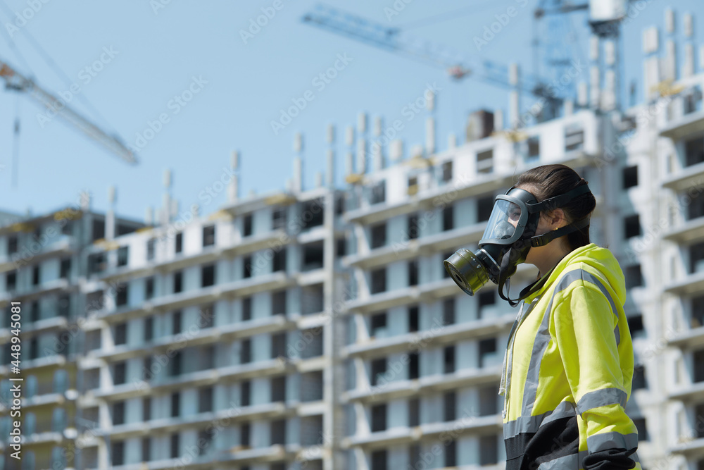 A girl in a green uniform and a gas mask on the background of a residential building under construction. Environmental Inspection A girl in a green uniform and a gas mask on the background of a residential building under construction. Environmental Inspection