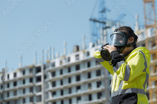 An employee of the gas and environmental inspection puts on a gas mask against the background of an industrial unfinished building