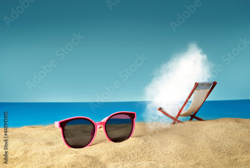 Pink glasses on the sand close up. Glasses on a beach chair background. Beach chairs on a background of blue water and sky. White cloud sunbathes on the beach.