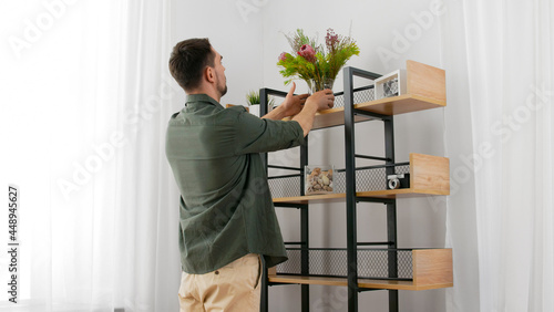 home improvement, decoration and people concept - happy smiling man placing flowers in vase to shelf