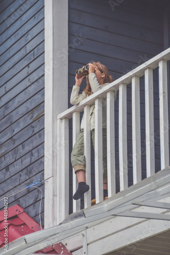 the child girl looks through binoculars standing on the balcony of the house © dmitrypk