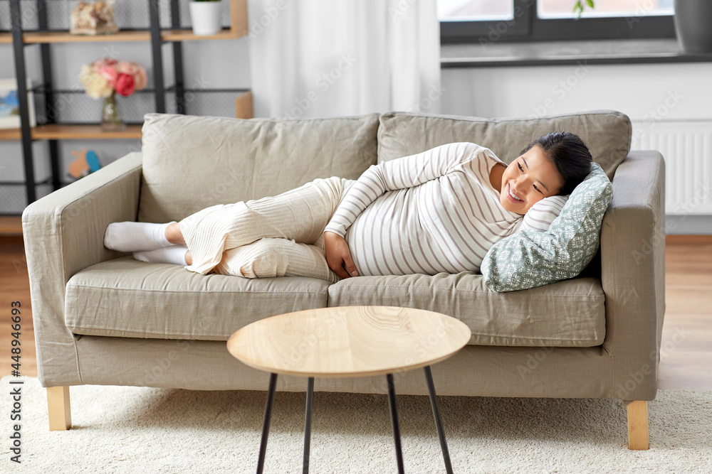pregnancy, rest, people and expectation concept - happy smiling pregnant asian woman lying on sofa at home
