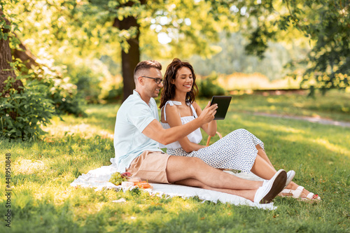 leisure and people concept - happy couple with tablet pc computer having picnic at summer park