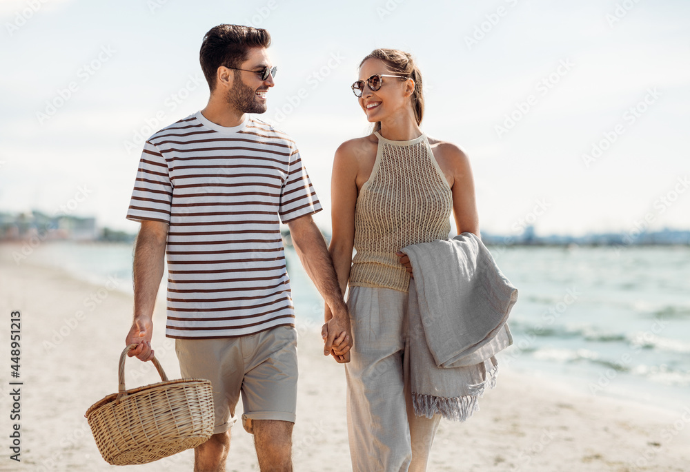 © Syda Productions - leisure, relationships and people concept - happy couple with picnic basket and blanket walking along beach