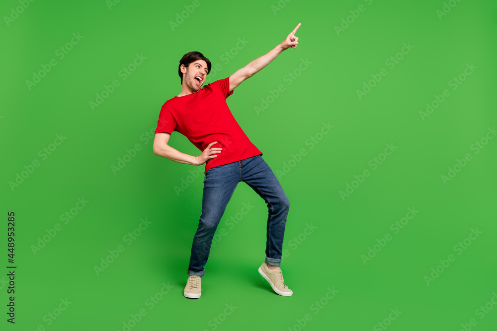 Photo of excited crazy guy dance direct finger empty space wear red t-shirt isolated green color background Photo of excited crazy guy dance direct finger empty space wear red t-shirt isolated green color background