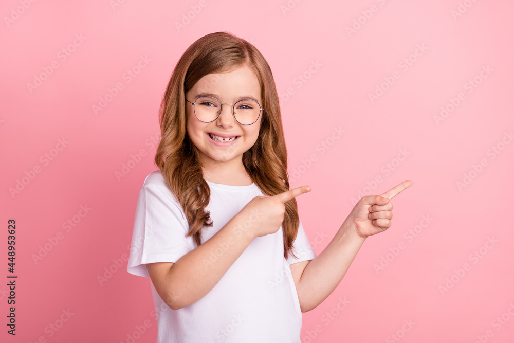 Photo of promoter small girl direct finger empty space wear eyewear white t-shirt isolated pink color background Photo of promoter small girl direct finger empty space wear eyewear white t-shirt isolated pink color background