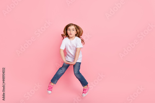 Photo of shocked funny girl jump omg reaction wear spectacles white t-shirt jeans isolated pink color background