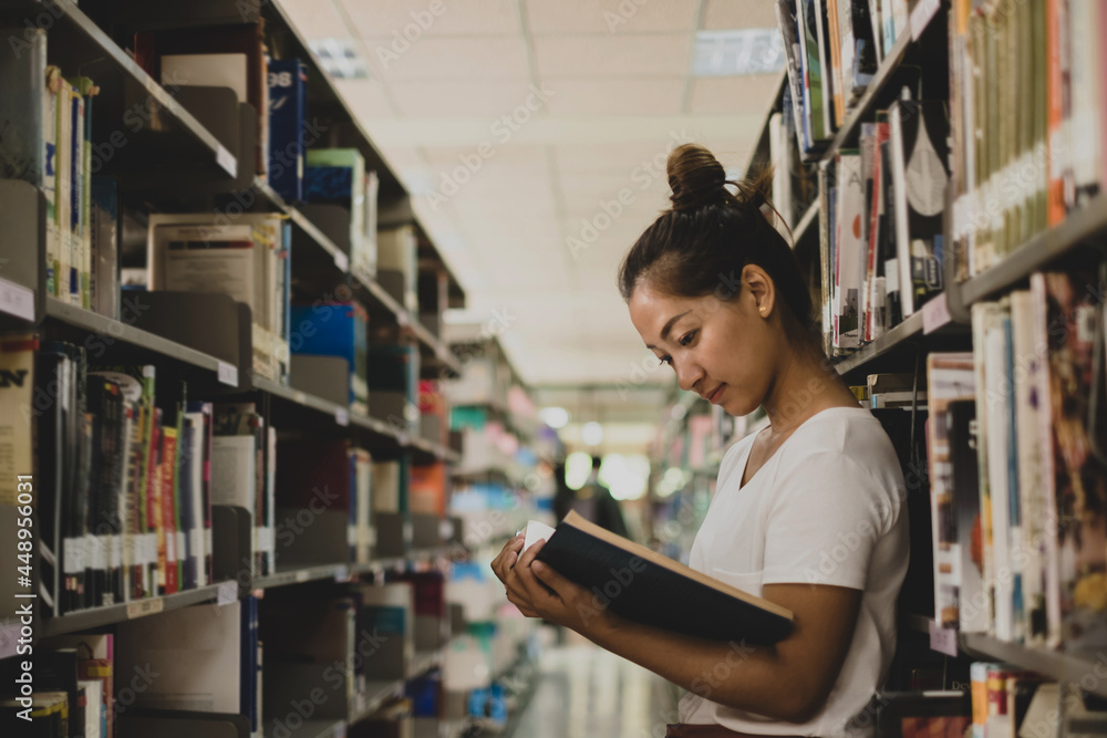 Young Asian women are searching for books and reading books on the tables and aisles of the college libraries to research and develop their academic and education self Young Asian women are searching for books and reading books on the tables and aisles of the college libraries to research and develop their academic and education self