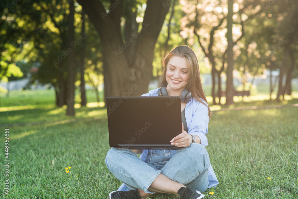 A young and attractive girl in headphones sitting on the grass on the lawn. Diastance working. Freelance, blogging concept A young and attractive girl in headphones sitting on the grass on the lawn. Diastance working. Freelance, blogging concept