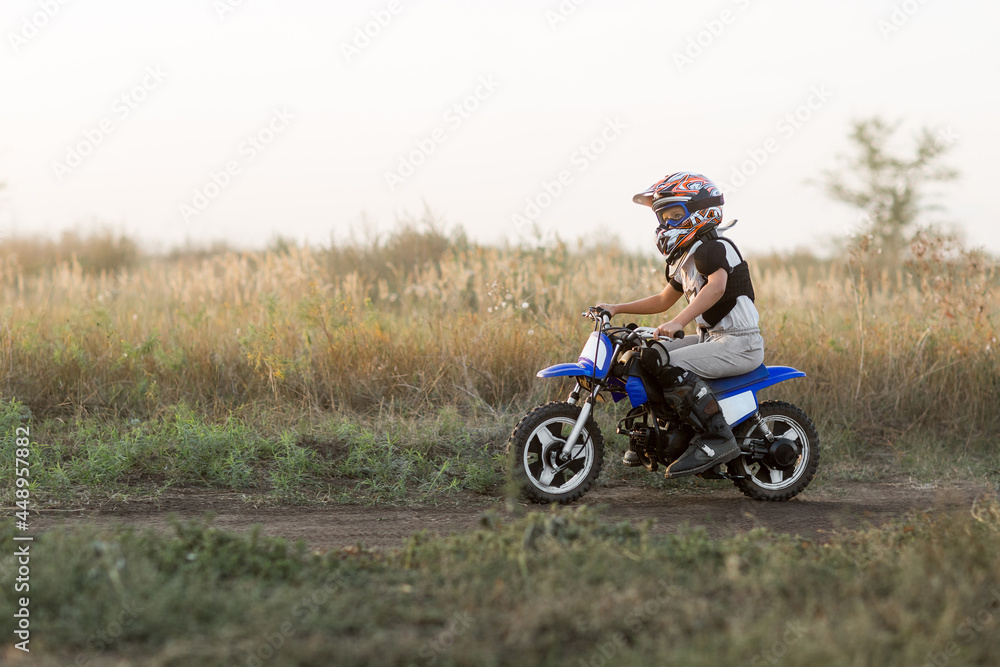 Child on his small motorcycle. Small biker dressed in a protective suit and helmet. The kid is engaged in motocross. Child on his small motorcycle. Small biker dressed in a protective suit and helmet. The kid is engaged in motocross.