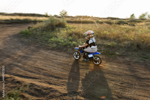 Fototapeta Naklejka Na Ścianę i Meble -  Child on his small motorcycle. Small biker dressed in a protective suit and helmet. The kid is engaged in motocross.